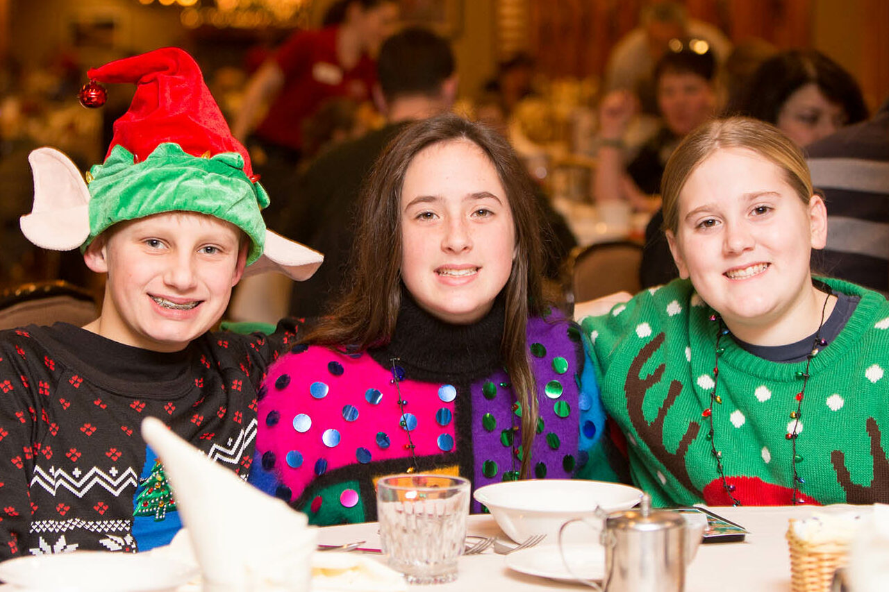 Three young people at a dining table wearing christmas sweaters.