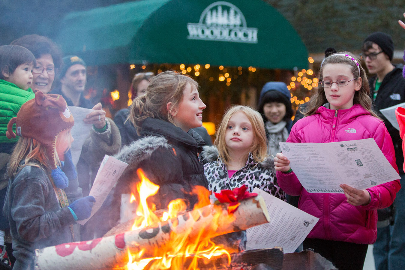 Young people reading menus outdoors next to Yule log fire.