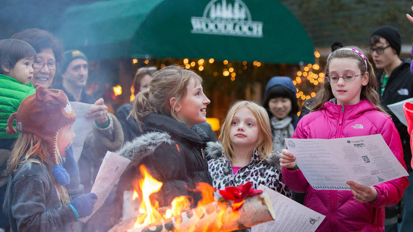 Young people reading menus outdoors next to Yule log fire.